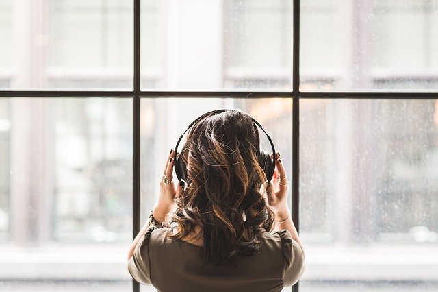 Girl wearing headphones recording a podcast while looking out of a window.